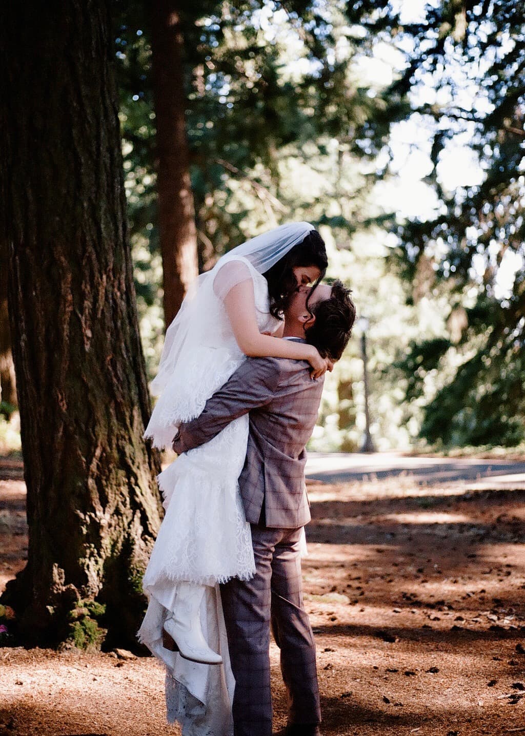 A groom lifts his bride for a kiss in a redwood grove